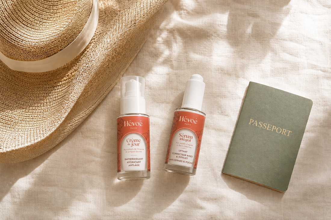 Soins visage naturels Hévoé disposés pour un voyage : sérum, nettoyant et accessoires de vacances sur lin crème